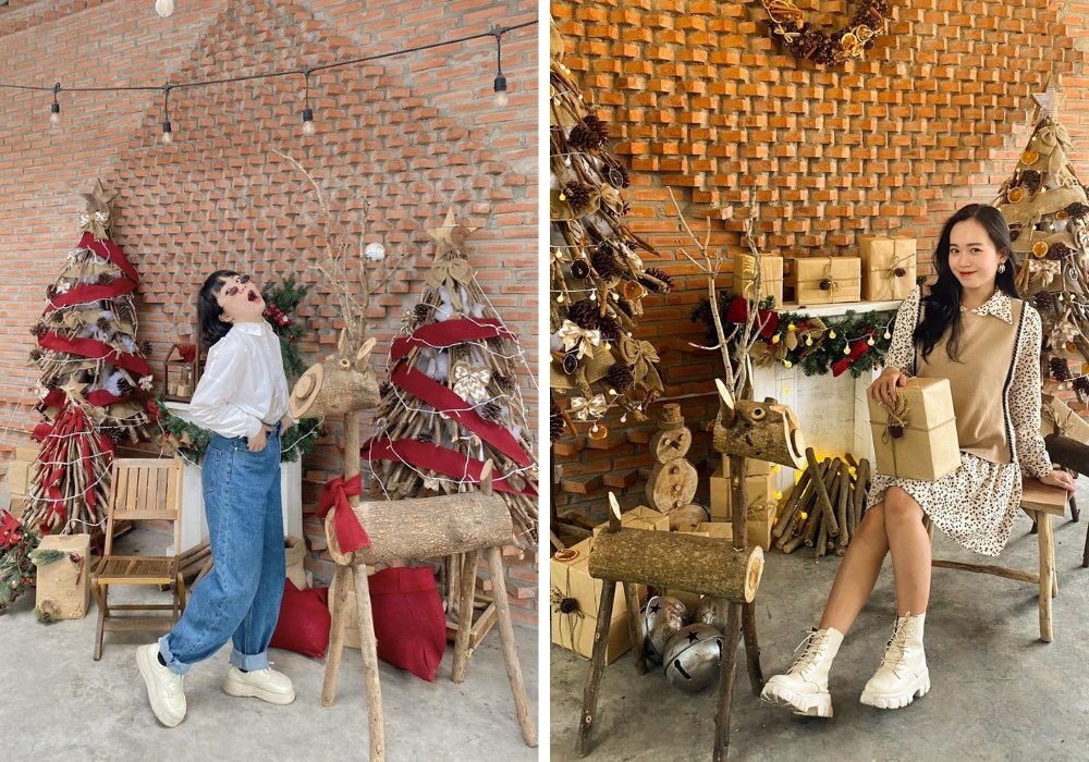 Hai người tạo dáng trước cảnh Giáng sinh với cây thông, tuần lộc gỗ và quà tặng, nền tường gạch.