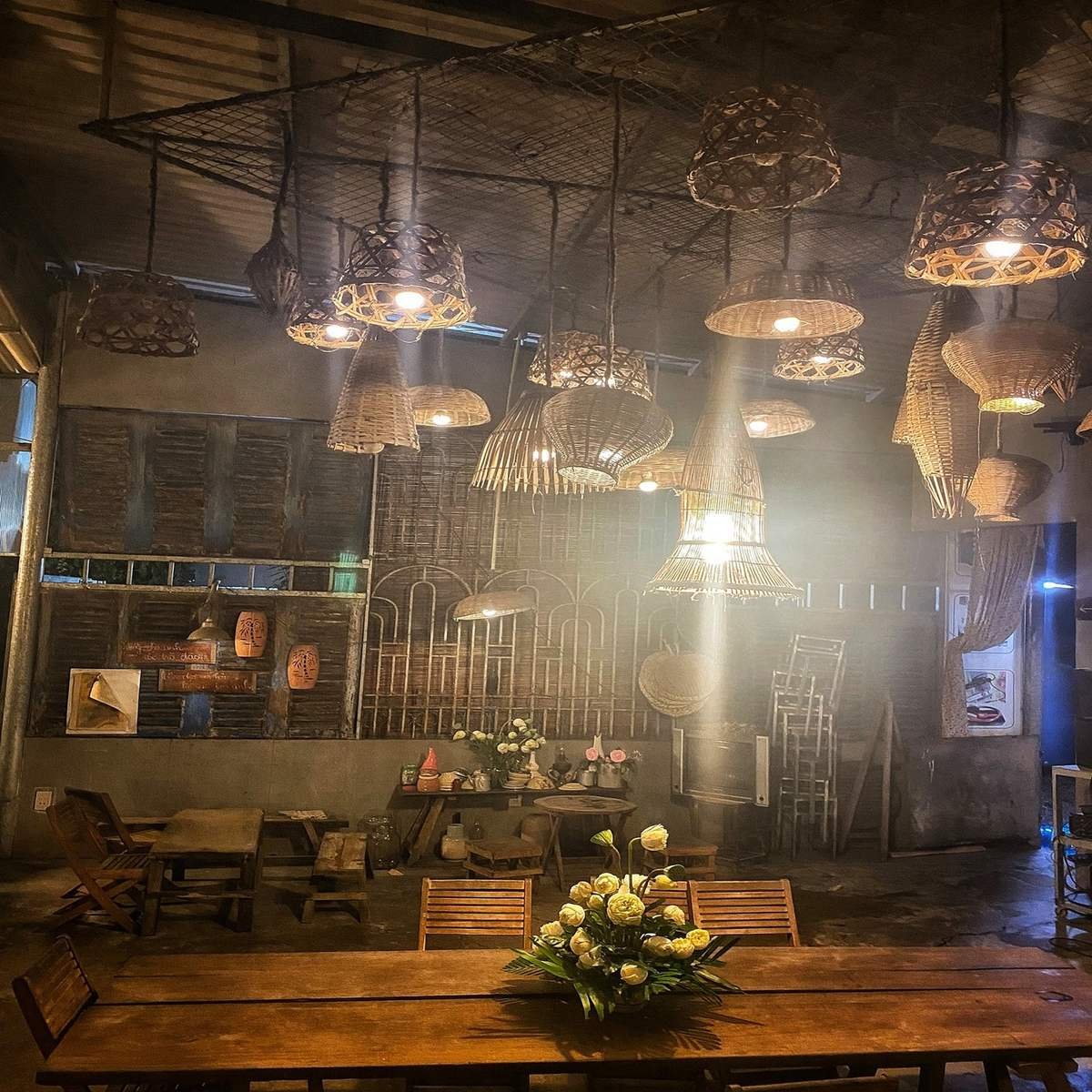 Kh&ocirc;ng gian nội thất với đ&egrave;n treo bằng tre, b&agrave;n gỗ d&agrave;i v&agrave; hoa trang tr&iacute; trong &aacute;nh s&aacute;ng ấm &aacute;p.