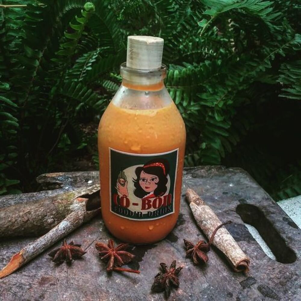 Chai nước m&agrave;u cam c&oacute; nh&atilde;n h&igrave;nh ảnh, đặt tr&ecirc;n bề mặt gỗ c&ugrave;ng với quế v&agrave; hoa hồi.