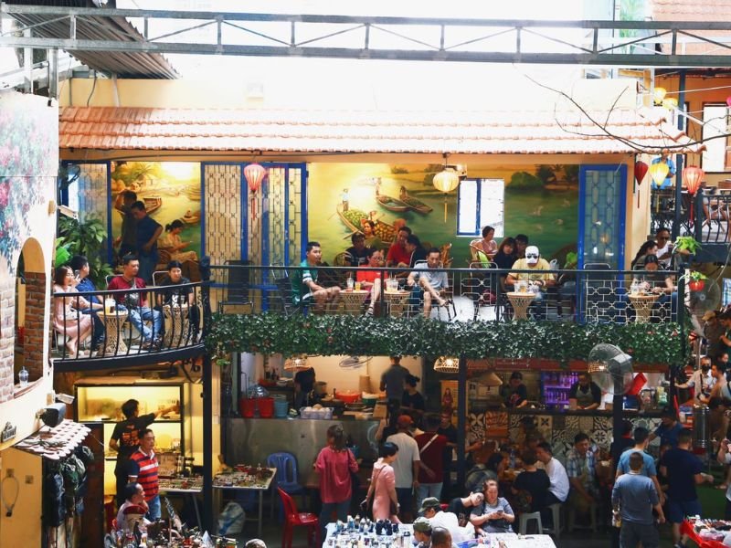 Qu&aacute;n c&agrave; ph&ecirc; hai tầng với kh&aacute;ch ngồi thưởng thức đồ uống, trang tr&iacute; tường bằng tranh v&agrave; đ&egrave;n lồng nhiều m&agrave;u sắc.