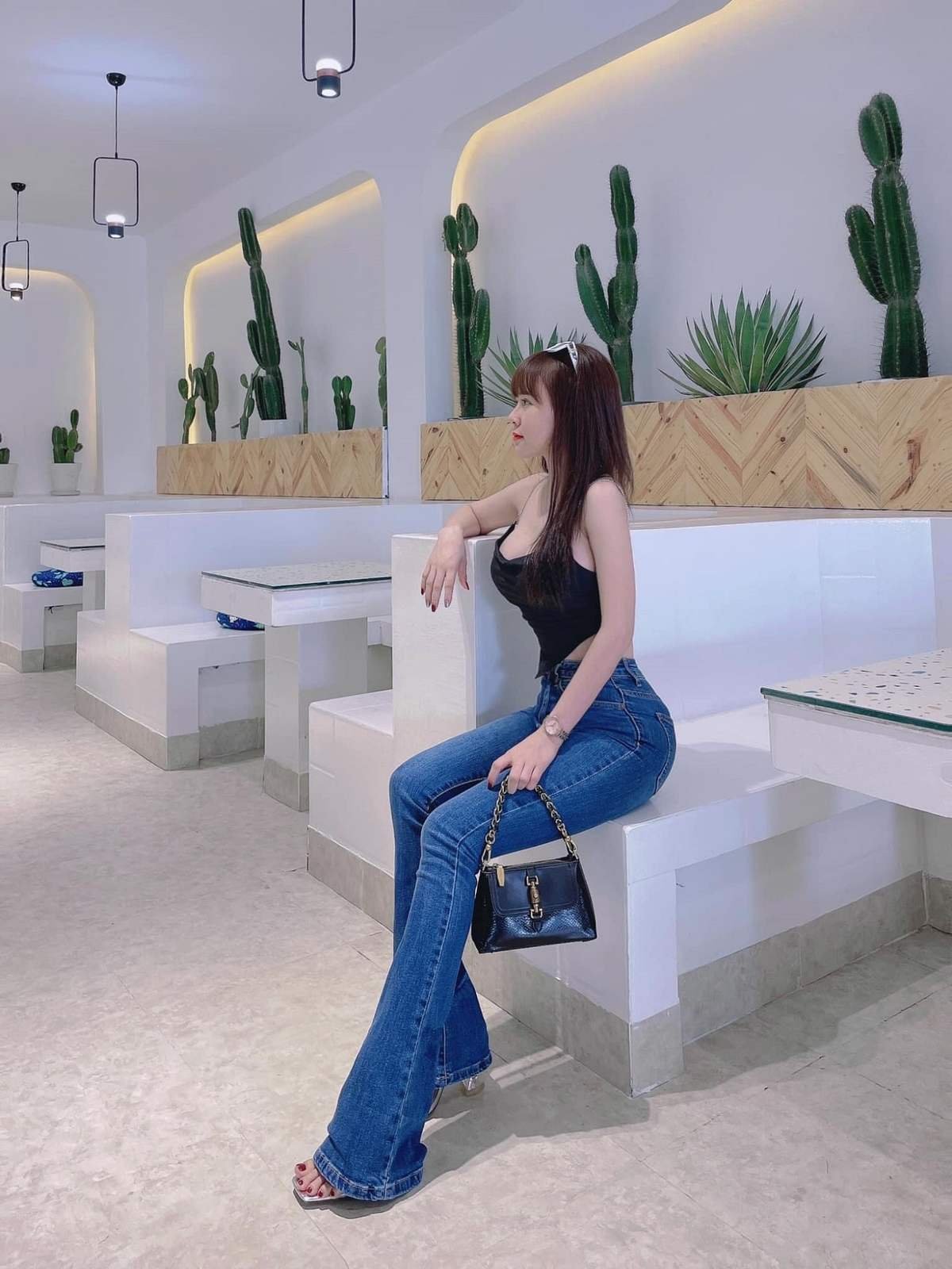 Người phụ nữ ngồi trong qu&aacute;n c&agrave; ph&ecirc; với thiết kế hiện đại, xung quanh c&oacute; nhiều c&acirc;y xương rồng trang tr&iacute;.