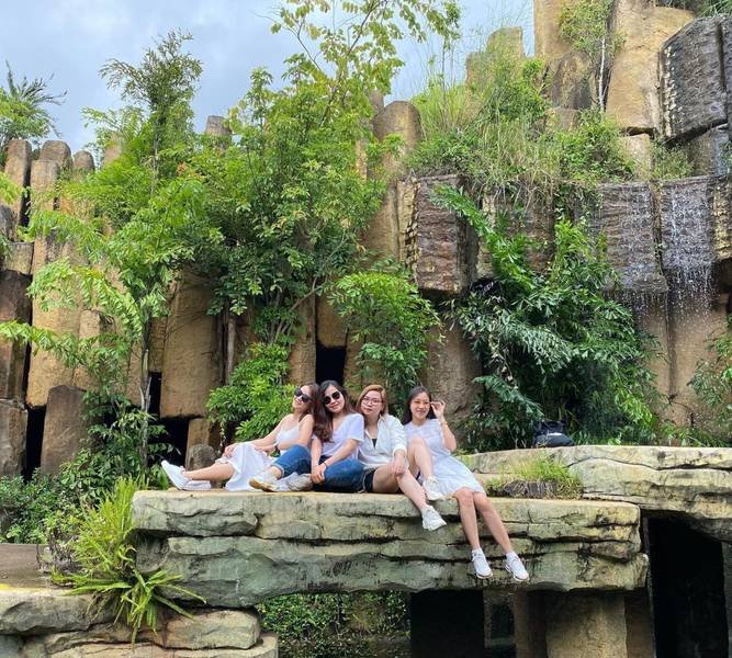 Bốn người ngồi tr&ecirc;n tảng đ&aacute; lớn trước khung cảnh thi&ecirc;n nhi&ecirc;n xanh tươi với c&acirc;y cối v&agrave; cấu tr&uacute;c đ&aacute;.