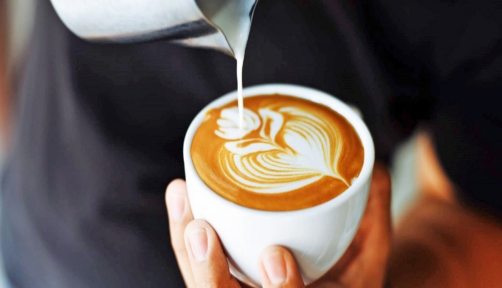latte-art-la-gi Người cầm tách cà phê với hình vẽ nghệ thuật từ sữa đang được rót vào.