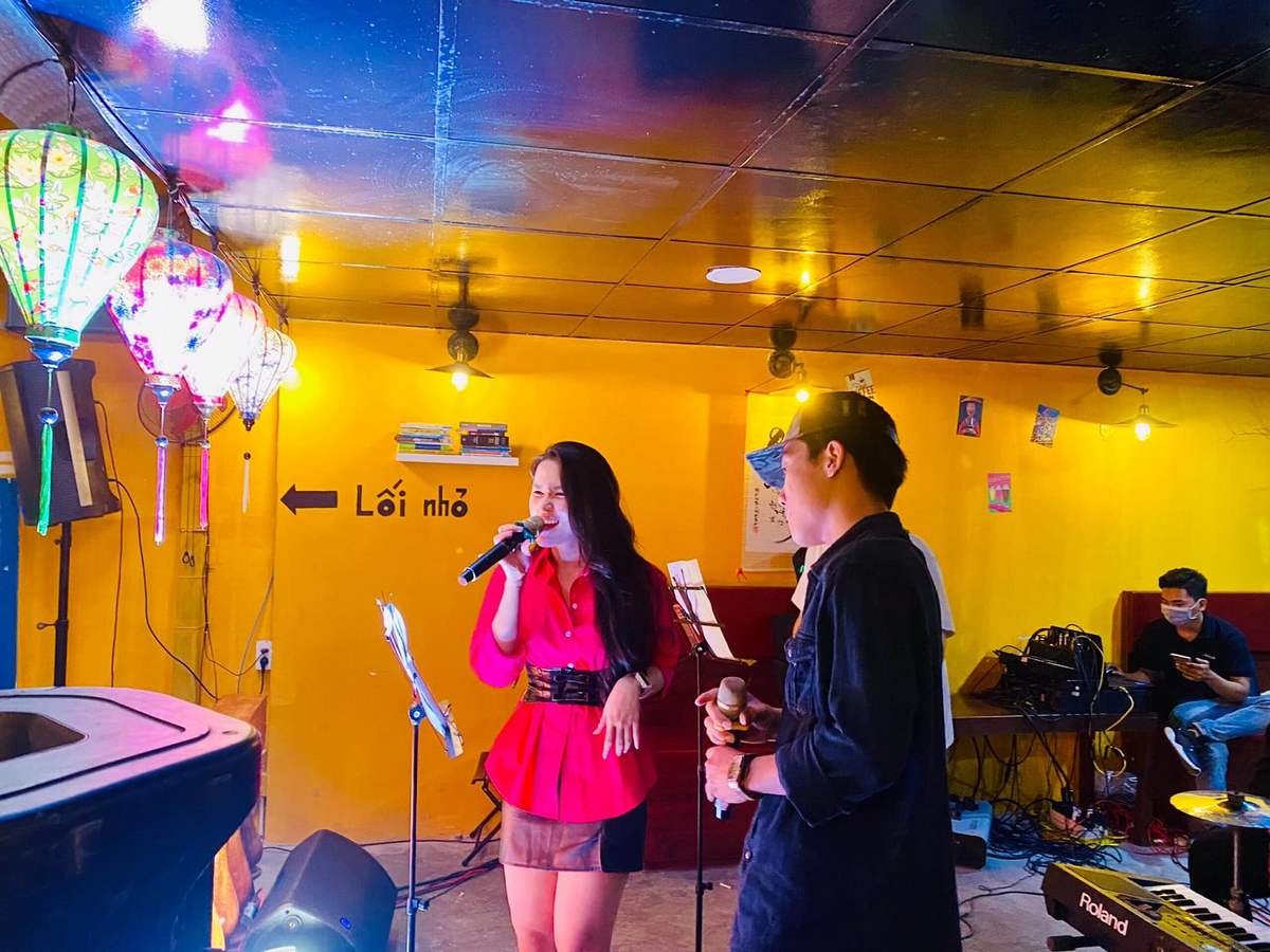 Người phụ nữ v&agrave; người đ&agrave;n &ocirc;ng đang h&aacute;t tr&ecirc;n s&acirc;n khấu nhỏ, xung quanh c&oacute; đ&egrave;n lồng v&agrave; nhạc cụ.