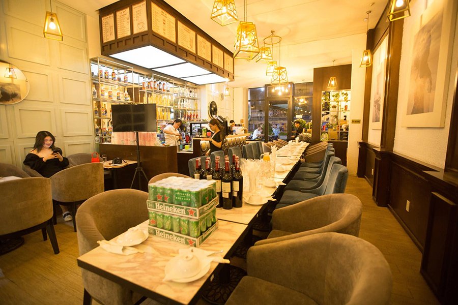 Qu&aacute;n c&agrave; ph&ecirc; với kh&ocirc;ng gian ấm c&uacute;ng, b&agrave;n ghế b&agrave;y biện sẵn, đ&egrave;n treo v&agrave; kệ rượu ph&iacute;a sau quầy pha chế.