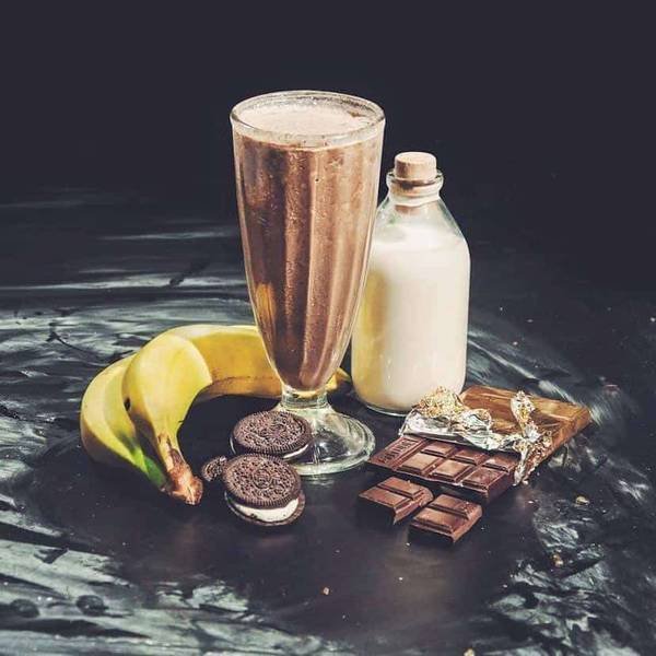 Ly sinh tố socola, sữa trong chai, chuối, b&aacute;nh quy v&agrave; thanh socola tr&ecirc;n nền đen.