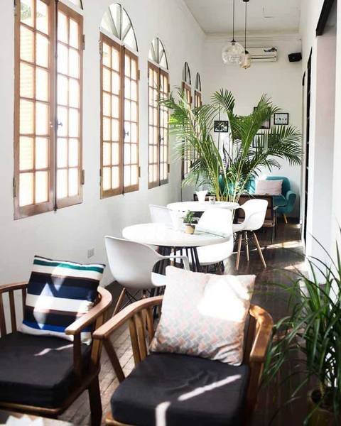 Qu&aacute;n c&agrave; ph&ecirc; s&aacute;ng sủa với b&agrave;n ghế gỗ, cửa sổ lớn, c&acirc;y xanh trang tr&iacute;, v&agrave; &aacute;nh s&aacute;ng tự nhi&ecirc;n chiếu v&agrave;o.