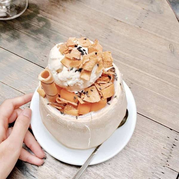 Ly kem dừa trang tr&iacute; với b&aacute;nh quế, dưa lưới v&agrave; hạt m&egrave; đen tr&ecirc;n đĩa trắng, tay cầm b&ecirc;n cạnh.