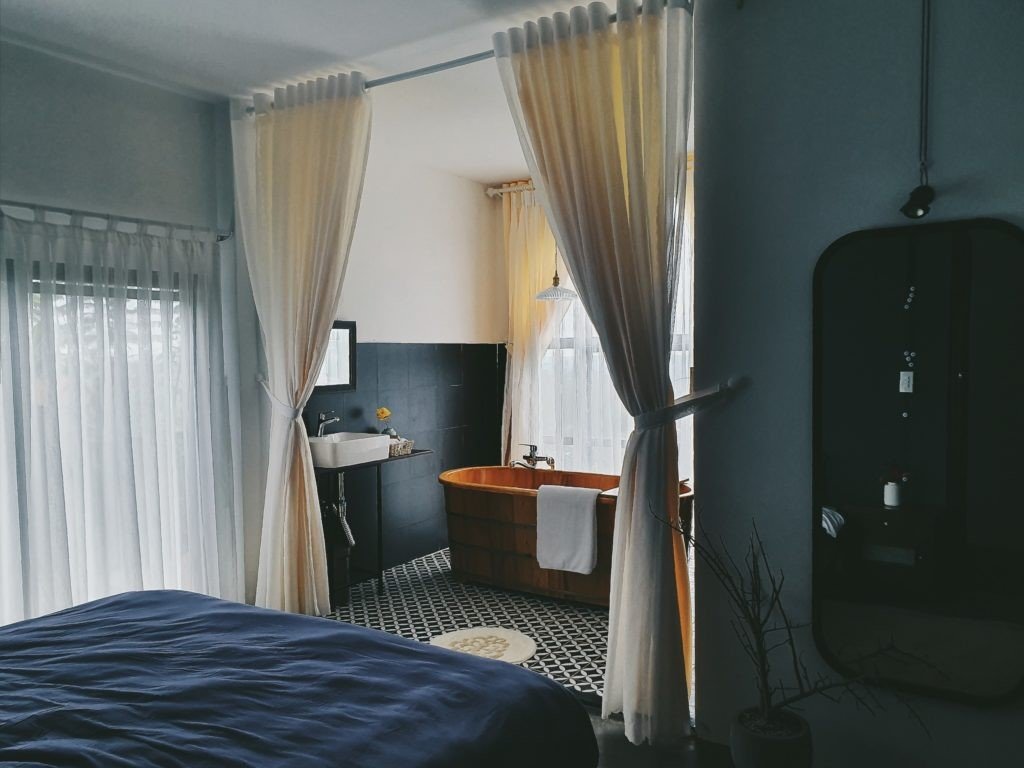 Ph&ograve;ng ngủ v&agrave; ph&ograve;ng tắm liền kề với bồn tắm gỗ, r&egrave;m trắng v&agrave; bồn rửa mặt, tạo kh&ocirc;ng gian ấm c&uacute;ng v&agrave; hiện đại.