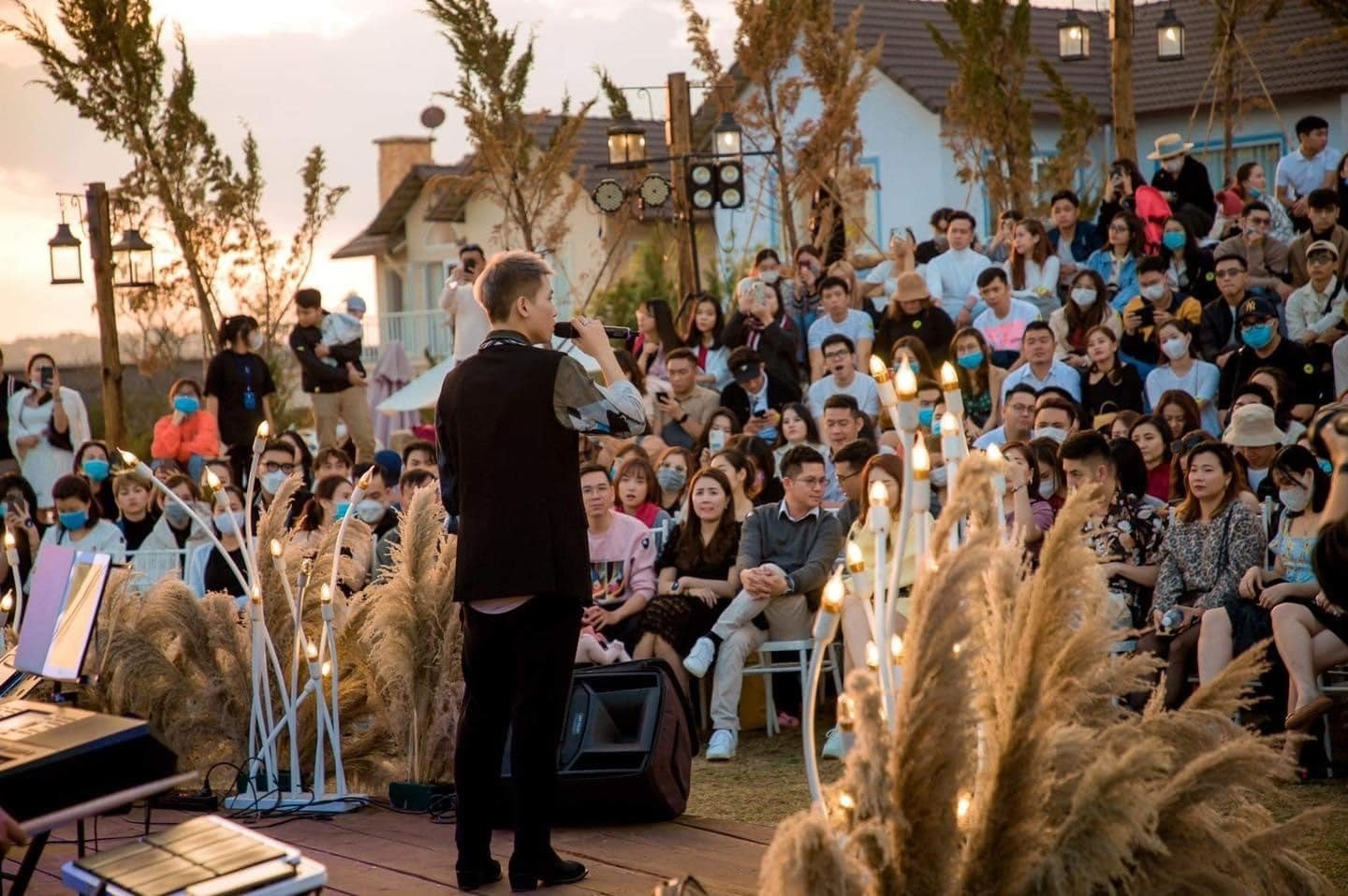 Người tr&igrave;nh diễn tr&ecirc;n s&acirc;n khấu ngo&agrave;i trời, kh&aacute;n giả ngồi xung quanh, &aacute;nh s&aacute;ng lung linh v&agrave;o l&uacute;c ho&agrave;ng h&ocirc;n.