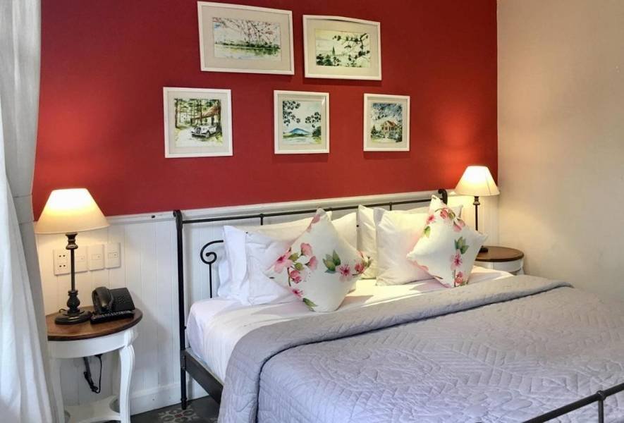 Ph&ograve;ng ngủ với giường đ&ocirc;i, tường đỏ trang tr&iacute; tranh, đ&egrave;n ngủ hai b&ecirc;n v&agrave; gối in hoa.