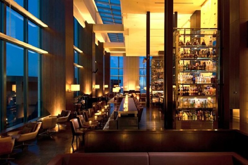 memory-lounge-da-nang-chiec-la-khong-lo-ben-canh-song-han-4-1636483013 Quầy bar sang trọng với ánh đèn ấm áp, kệ rượu lớn và cửa sổ cao nhìn ra bên ngoài vào buổi tối.