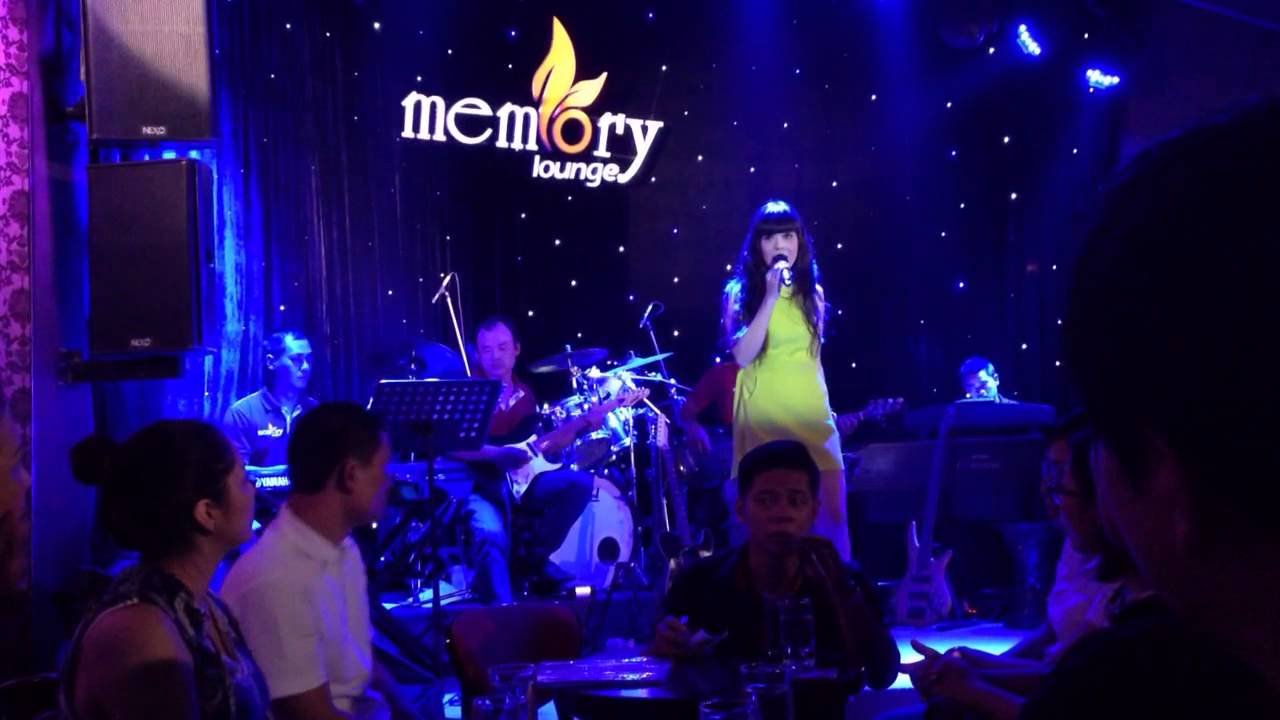 memory-lounge-da-nang-chiec-la-khong-lo-ben-canh-song-han-6-1636482662 Ca sĩ biểu diễn trên sân khấu với ban nhạc, khán giả ngồi thưởng thức trong không gian quán bar ánh sáng xanh.