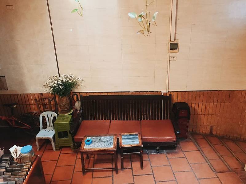 G&oacute;c ph&ograve;ng với ghế gỗ, b&agrave;n nhỏ, b&igrave;nh hoa, v&agrave; tường l&aacute;t gạch n&acirc;u, tạo cảm gi&aacute;c ấm c&uacute;ng v&agrave; giản dị.