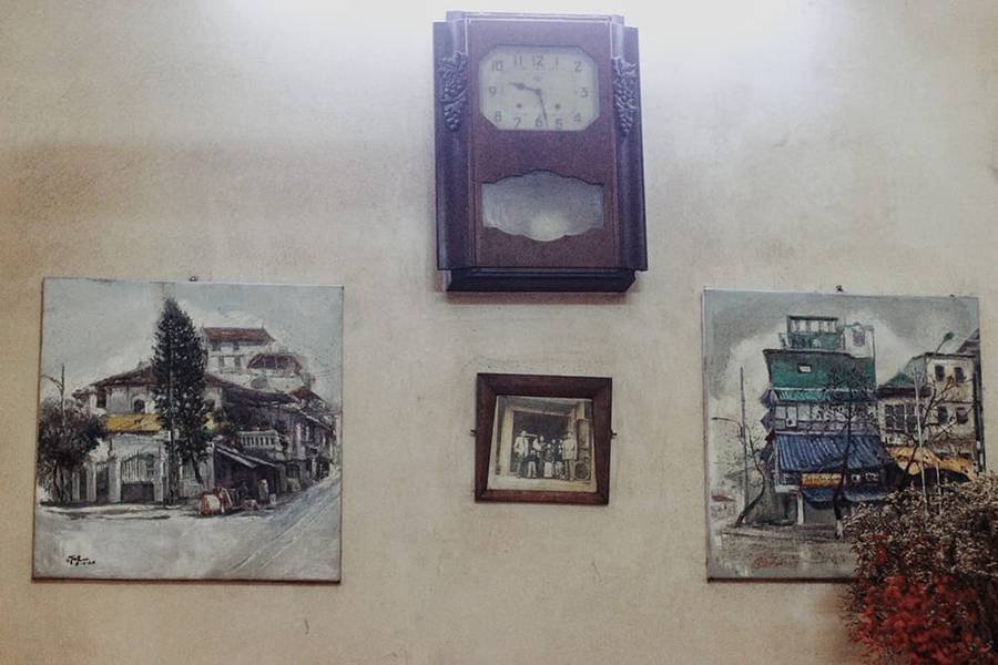 Đồng hồ treo tường v&agrave; ba bức tranh tr&ecirc;n nền tường trắng, gồm hai bức tranh phong cảnh v&agrave; một ảnh đen trắng.