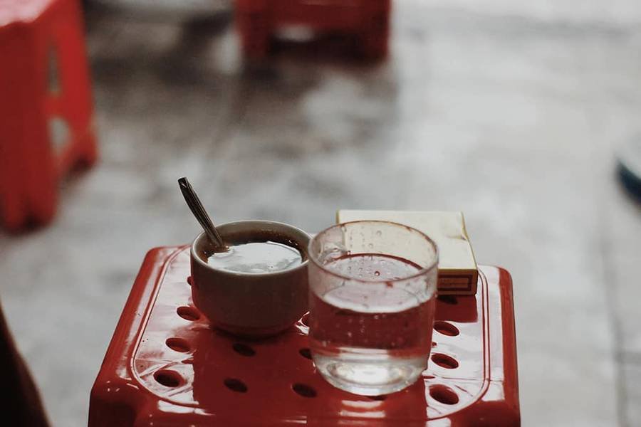 Ly nước, t&aacute;ch c&agrave; ph&ecirc; v&agrave; hộp giấy tr&ecirc;n ghế nhựa đỏ ngo&agrave;i trời.