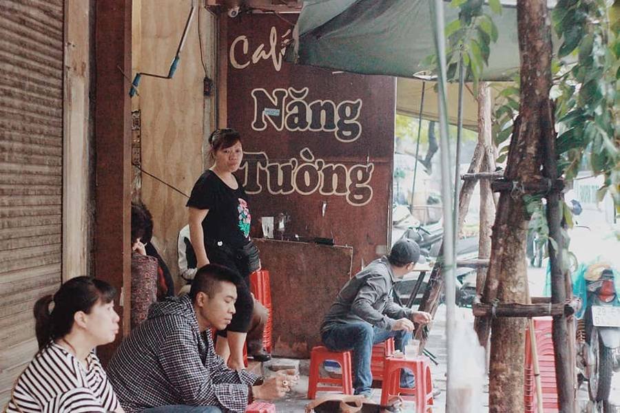 Nh&oacute;m người ngồi tr&ecirc;n ghế nhựa đỏ trước qu&aacute;n c&agrave; ph&ecirc; với biển hiệu "Năng Tường" tr&ecirc;n đường phố.