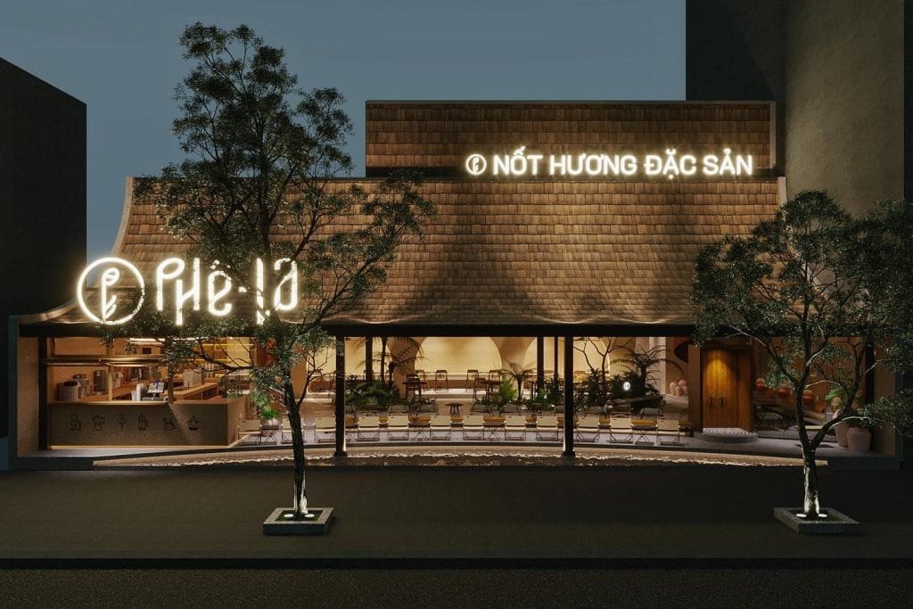 Mặt tiền quán cà phê với thiết kế gỗ, cây xanh và bảng hiệu sáng đèn vào buổi tối.