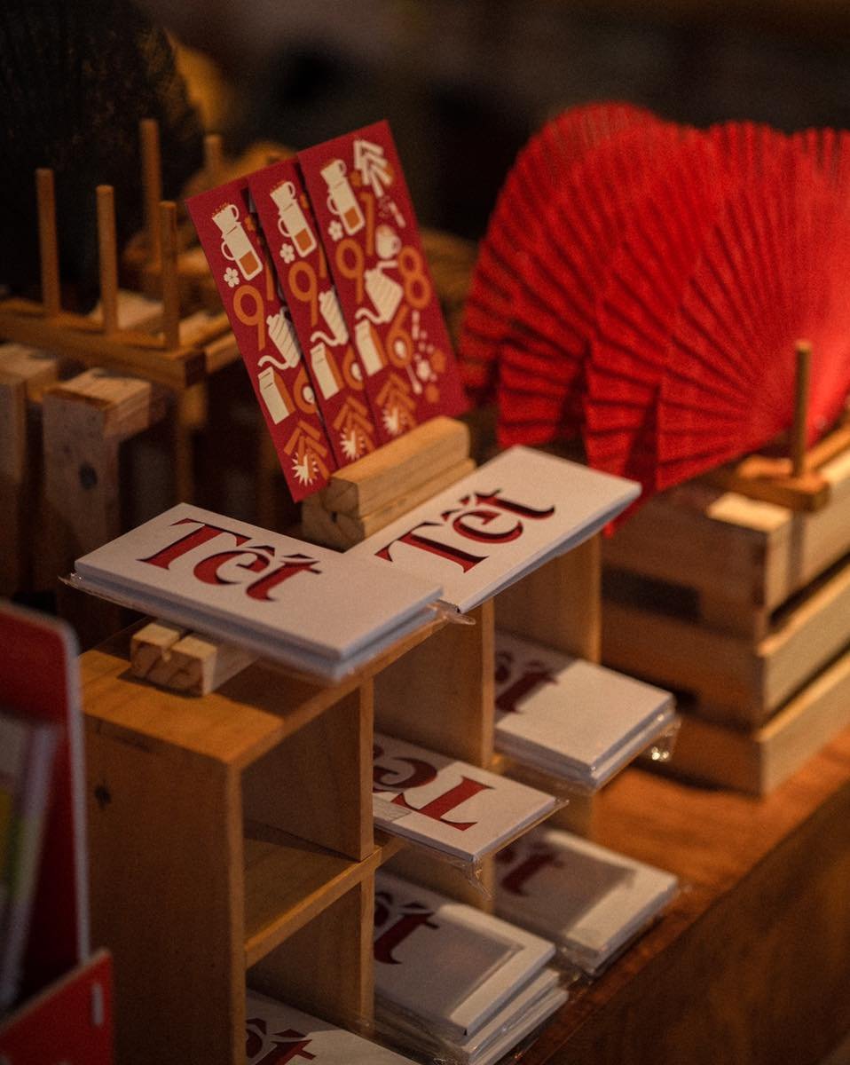 C&aacute;c tấm thiệp v&agrave; bao l&igrave; x&igrave; đỏ với chữ "Tết" được trưng b&agrave;y tr&ecirc;n kệ gỗ trong cửa h&agrave;ng.