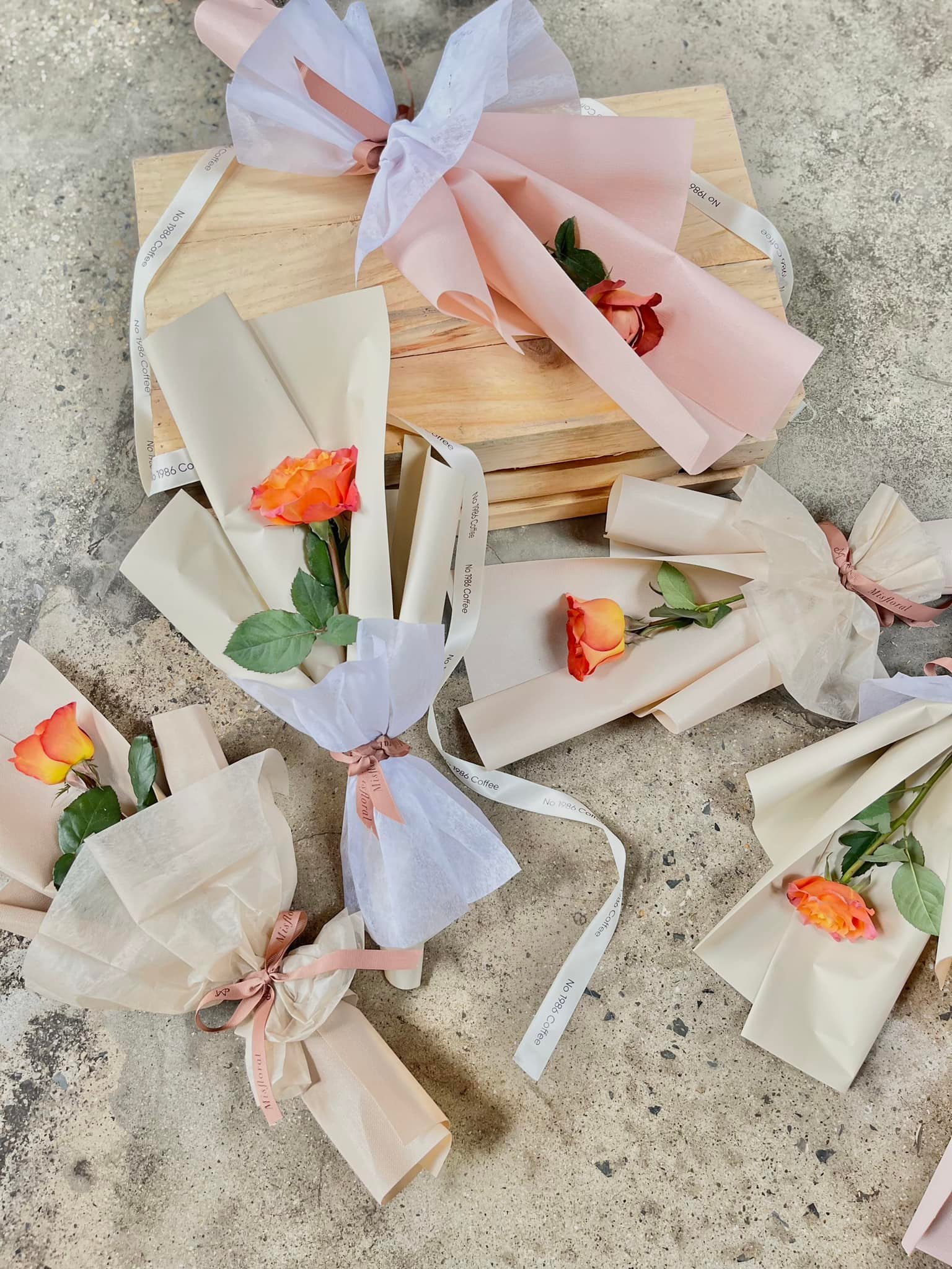 Những b&oacute; hoa hồng cam được g&oacute;i trong giấy m&agrave;u pastel v&agrave; đặt tr&ecirc;n nền xi măng.