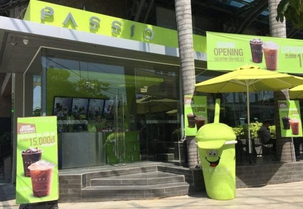 Top 32 thương hiệu nhượng quyền cafe siêu lợi nhuận 24 Quán cà phê với biển hiệu xanh lá, bảng quảng cáo đồ uống và mô hình ly nước đứng trước cửa.