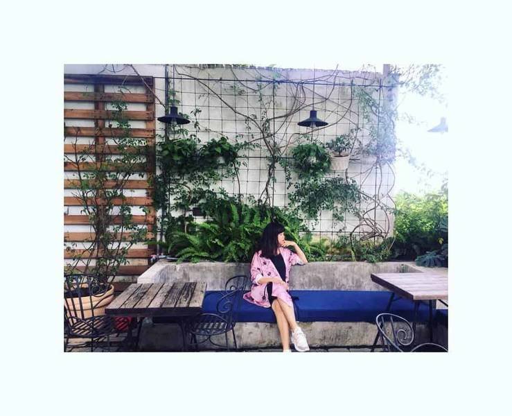 Người ngồi tr&ecirc;n ghế d&agrave;i trong qu&aacute;n c&agrave; ph&ecirc; ngo&agrave;i trời với tường c&acirc;y xanh v&agrave; b&agrave;n gỗ.