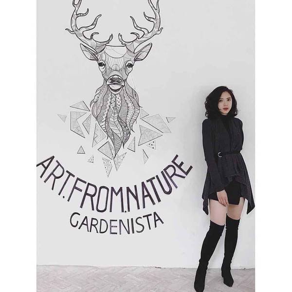 Người phụ nữ đứng cạnh bức tranh đầu hươu v&agrave; d&ograve;ng chữ "Art From Nature Gardenista" tr&ecirc;n tường trắng.