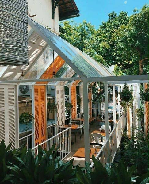 Qu&aacute;n c&agrave; ph&ecirc; ngo&agrave;i trời với m&aacute;i k&iacute;nh, b&agrave;n ghế gỗ, c&acirc;y xanh xung quanh, tạo kh&ocirc;ng gian tho&aacute;ng đ&atilde;ng v&agrave; thư gi&atilde;n.