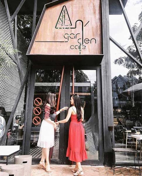 Hai người đứng trước cửa một qu&aacute;n c&agrave; ph&ecirc;, tr&ecirc;n biển hiệu c&oacute; d&ograve;ng chữ "garden cafe".