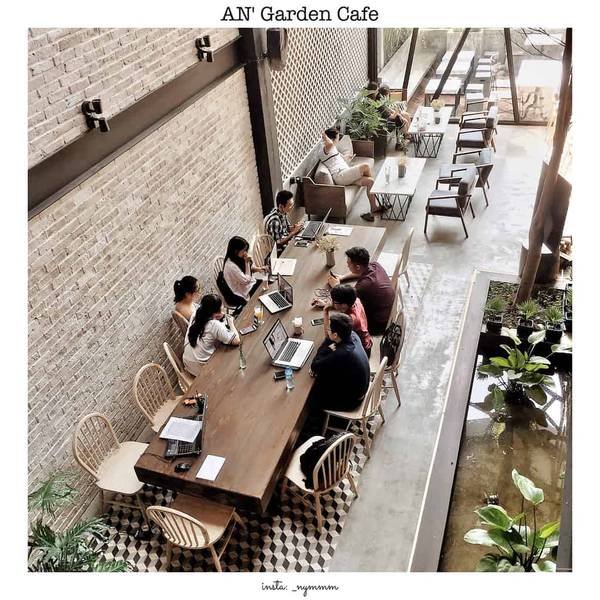 Một nh&oacute;m người đang l&agrave;m việc tr&ecirc;n m&aacute;y t&iacute;nh x&aacute;ch tay tại một qu&aacute;n c&agrave; ph&ecirc; với kh&ocirc;ng gian mở v&agrave; c&acirc;y xanh.