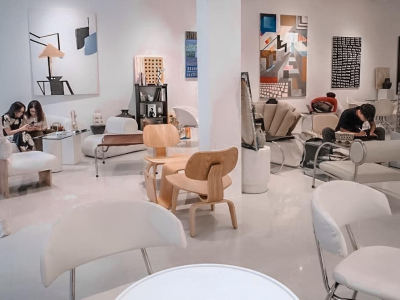 Phòng trưng bày nghệ thuật với nội thất hiện đại, tường treo tranh trừu tượng, vài người ngồi thư giãn và trò chuyện.