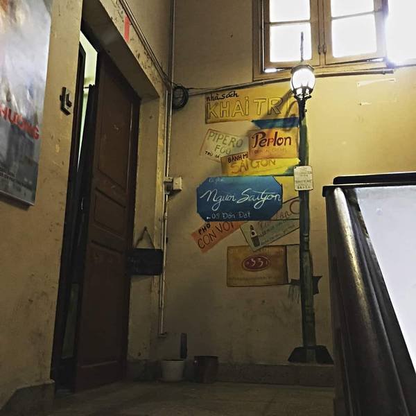 Cầu thang cũ với tường vẽ biển quảng c&aacute;o, cửa gỗ v&agrave; cửa sổ ph&iacute;a tr&ecirc;n, &aacute;nh s&aacute;ng từ đ&egrave;n b&ecirc;n cạnh.