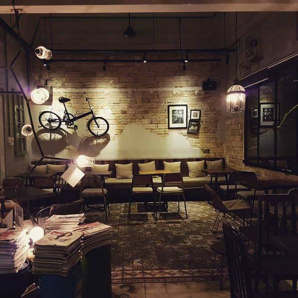 Qu&aacute;n c&agrave; ph&ecirc; với &aacute;nh s&aacute;ng ấm &aacute;p, xe đạp treo tường v&agrave; ghế sofa xếp quanh b&agrave;n gỗ, tạo cảm gi&aacute;c ấm c&uacute;ng.