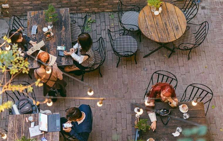 Qu&aacute;n c&agrave; ph&ecirc; ngo&agrave;i trời c&oacute; người ngồi tr&ograve; chuyện v&agrave; l&agrave;m việc, b&agrave;n ghế gỗ, &aacute;nh s&aacute;ng dịu nhẹ.