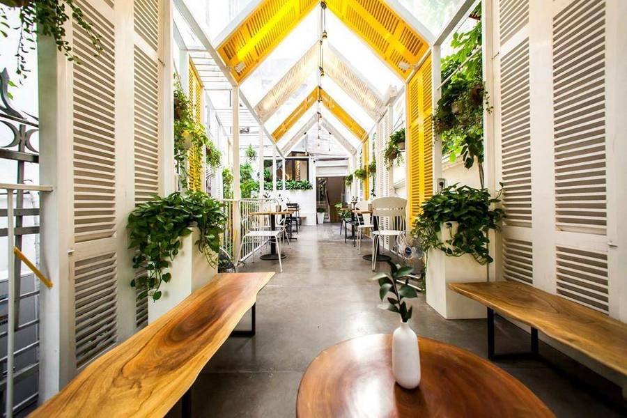 Qu&aacute;n c&agrave; ph&ecirc; trang tr&iacute; hiện đại với b&agrave;n ghế gỗ, c&acirc;y xanh treo tr&ecirc;n tường v&agrave; m&aacute;i k&iacute;nh lấy s&aacute;ng tự nhi&ecirc;n.