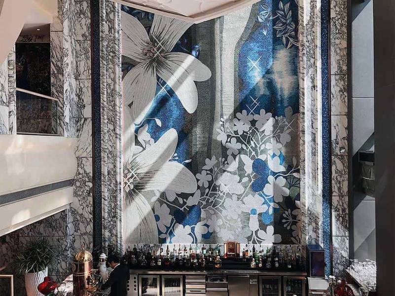Quầy bar với bức tranh tường hoa lớn, người pha chế đang l&agrave;m việc, kh&ocirc;ng gian nội thất sang trọng v&agrave; hiện đại.
