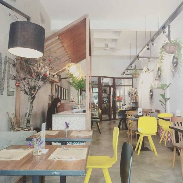 quan-cafe-dep-o-sai-gon-m2c-nadiapham Quán cà phê với bàn ghế gỗ, trang trí cây xanh và đèn treo, tạo không gian ấm cúng và hiện đại.