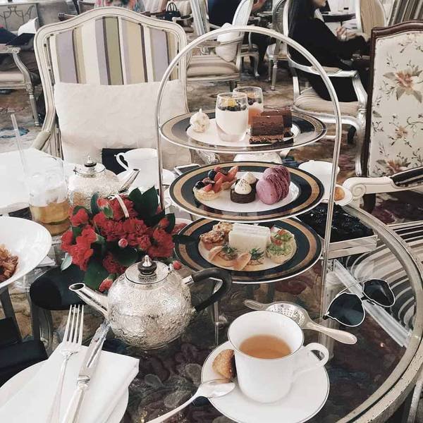 B&agrave;n tr&agrave; chiều với khay ba tầng chứa b&aacute;nh ngọt, tr&agrave; v&agrave; đồ trang tr&iacute; tại một qu&aacute;n c&agrave; ph&ecirc; sang trọng.