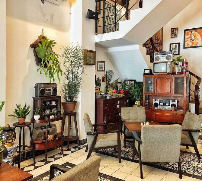 Qu&aacute;n c&agrave; ph&ecirc; nhỏ với nội thất cổ điển, b&agrave;n ghế gỗ, c&acirc;y xanh v&agrave; đ&agrave;i cassette trang tr&iacute;.