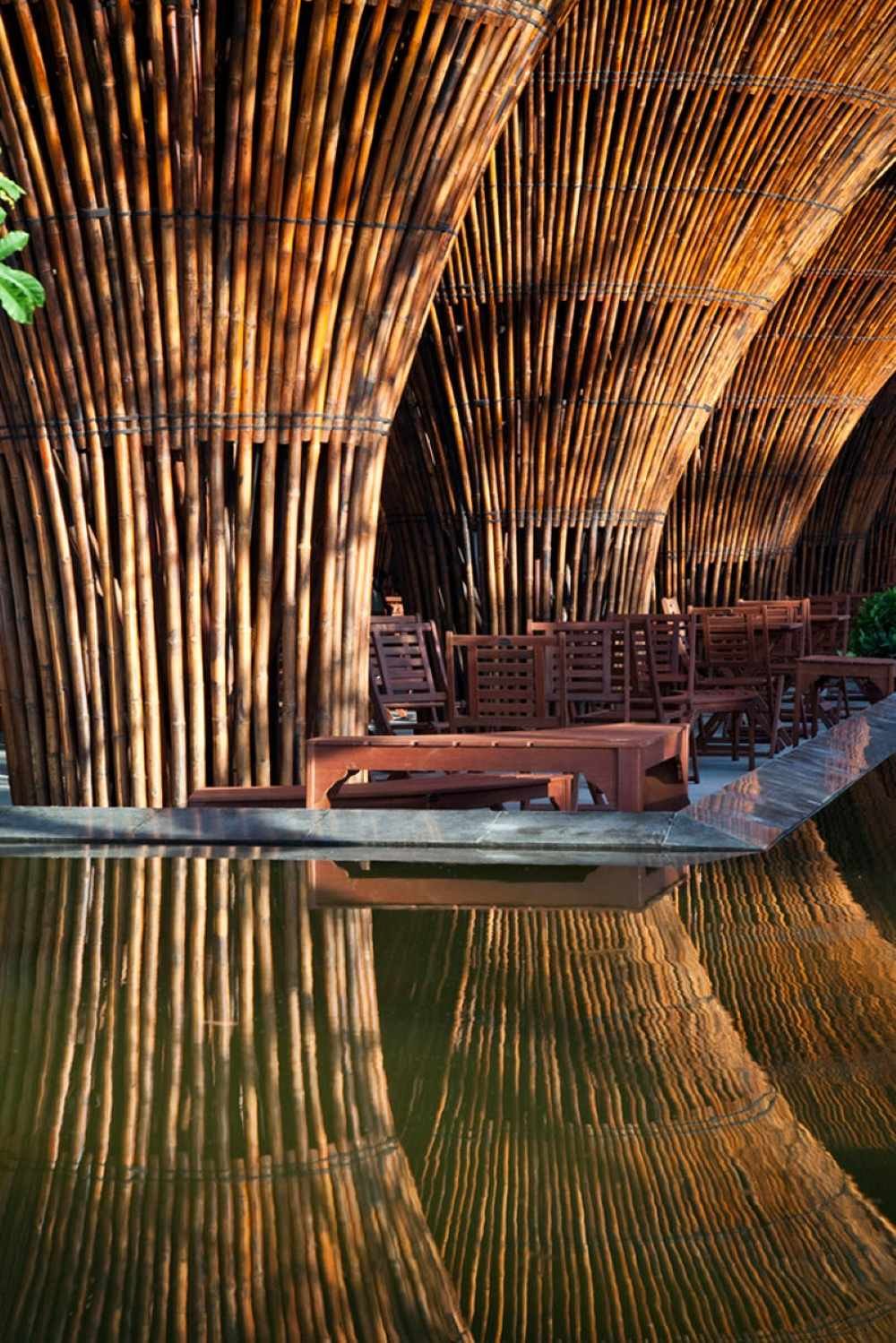 Cấu tr&uacute;c tre lớn với ghế gỗ b&ecirc;n dưới, phản chiếu tr&ecirc;n mặt nước tạo n&ecirc;n một khung cảnh y&ecirc;n b&igrave;nh.