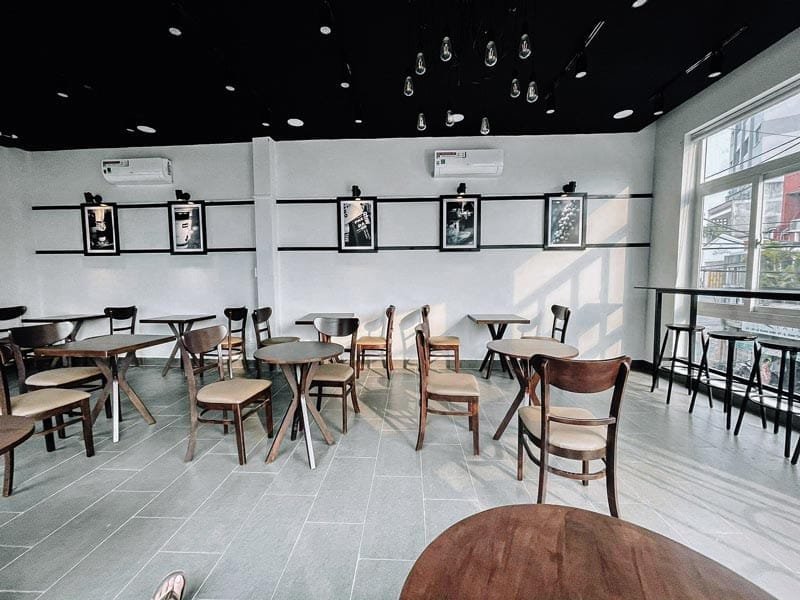 Nhượng quyền cafe Milano có chi phí bao nhiêu? Có nên không? 10 Quán cà phê với bàn ghế gỗ, tường trang trí tranh ảnh, ánh sáng tự nhiên chiếu qua cửa sổ lớn.