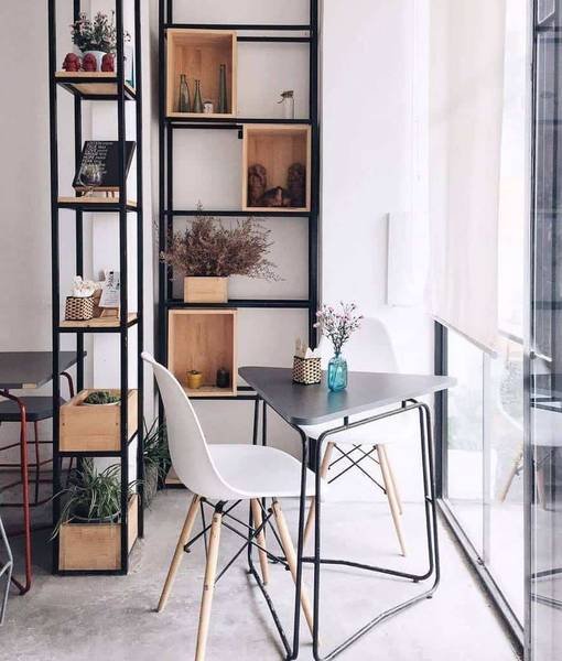 Quán cà phê với bàn ghế hiện đại, kệ sách và cây xanh tạo không gian thoáng đãng, sáng sủa.