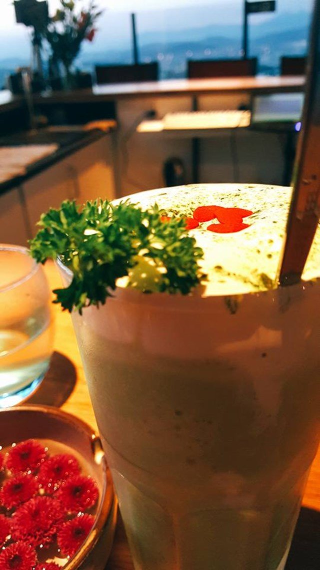 Ly đồ uống xanh l&aacute; c&acirc;y trang tr&iacute; c&agrave;nh rau m&ugrave;i t&acirc;y v&agrave; trang tr&iacute; đỏ, b&ecirc;n cạnh l&agrave; b&aacute;t nước c&oacute; hoa đỏ.