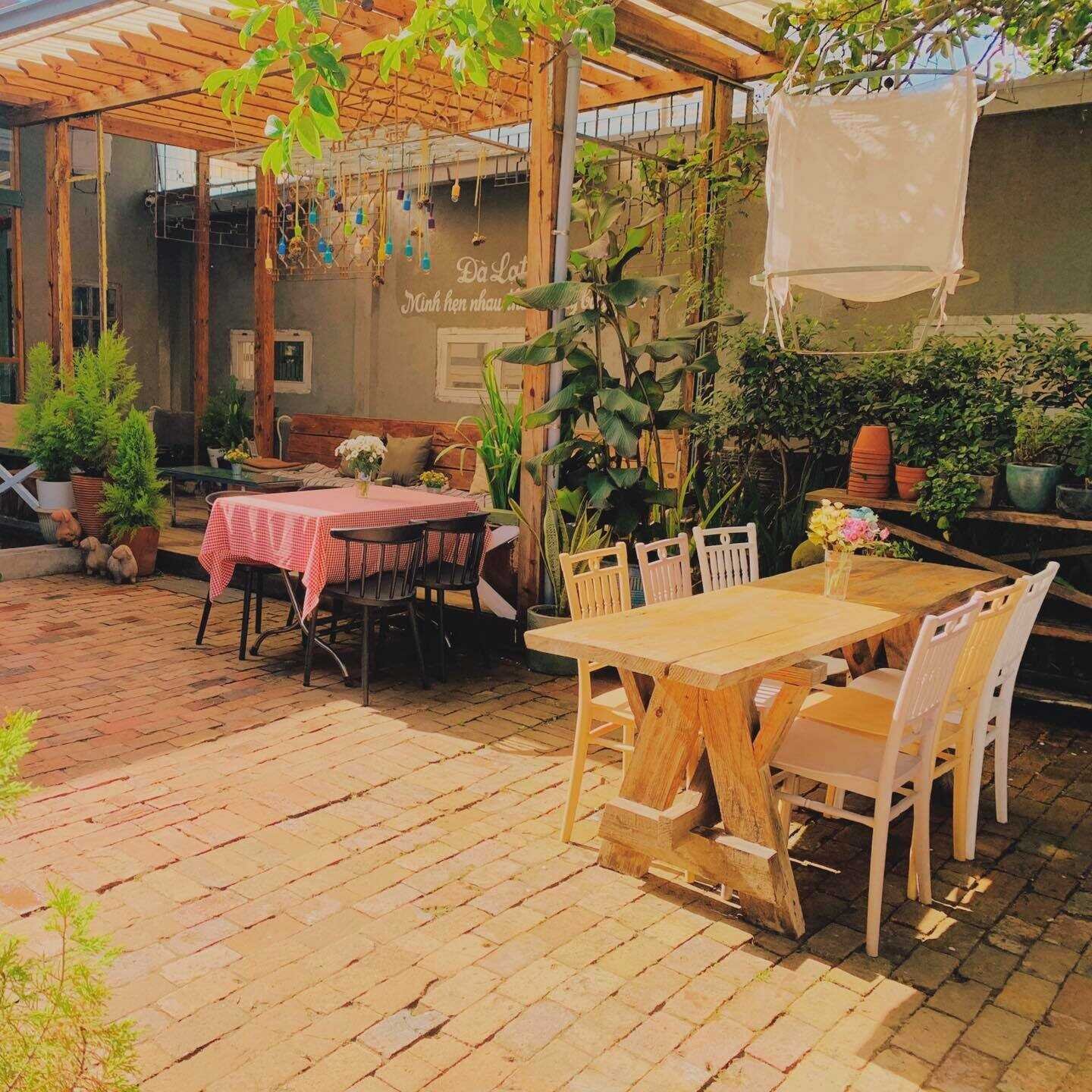 Khu vườn nhỏ với b&agrave;n ghế gỗ, c&acirc;y xanh v&agrave; &aacute;nh s&aacute;ng tự nhi&ecirc;n từ m&aacute;i che, tạo kh&ocirc;ng gian thư gi&atilde;n ngo&agrave;i trời.