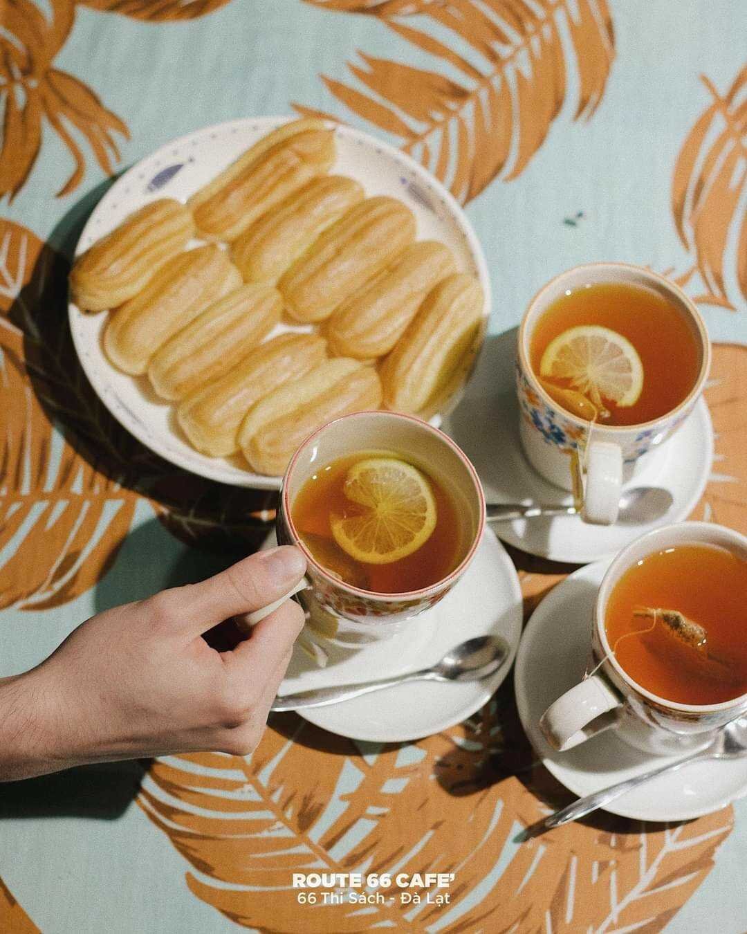 Ba t&aacute;ch tr&agrave; với l&aacute;t chanh tr&ecirc;n b&agrave;n, b&ecirc;n cạnh đĩa b&aacute;nh ngọt nhỏ. Một tay đang cầm một t&aacute;ch tr&agrave;.