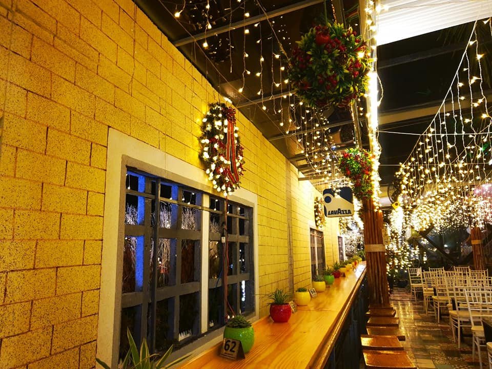 Qu&aacute;n c&agrave; ph&ecirc; được trang tr&iacute; đ&egrave;n lấp l&aacute;nh, tường gạch v&agrave;ng, chậu c&acirc;y v&agrave; v&ograve;ng hoa treo tr&ecirc;n trần.