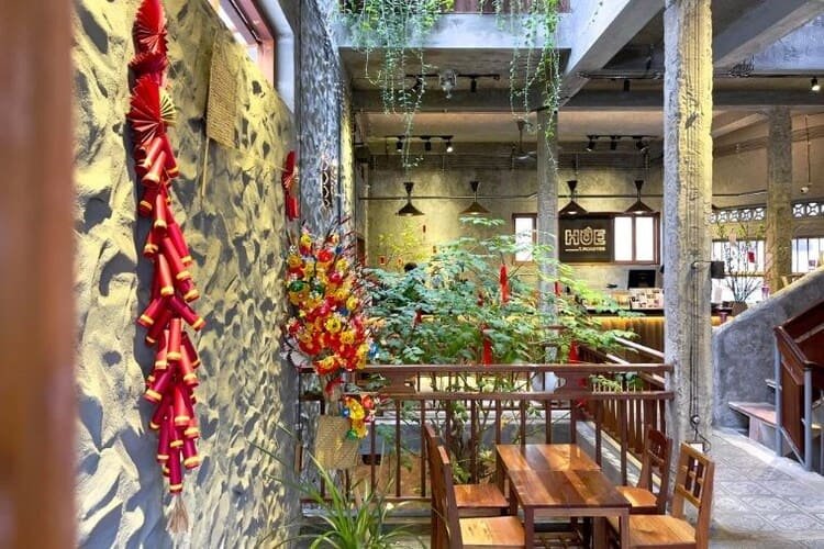 Qu&aacute;n c&agrave; ph&ecirc; trang tr&iacute; Tết với c&acirc;y xanh, đ&egrave;n lồng đỏ v&agrave; b&agrave;n ghế gỗ.