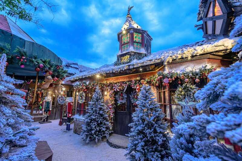 Khu vườn phủ đầy tuyết với c&acirc;y th&ocirc;ng v&agrave; trang tr&iacute; Gi&aacute;ng Sinh lung linh dưới bầu trời xanh s&aacute;ng.