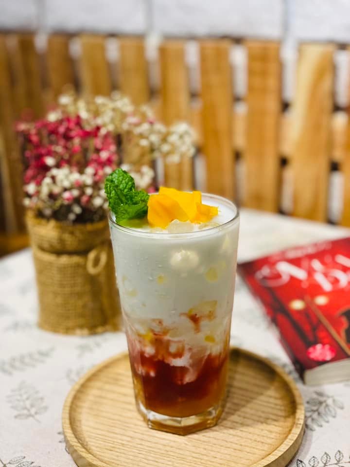 Ly đồ uống với lớp kem, sốt d&acirc;u, trang tr&iacute; l&aacute; bạc h&agrave; v&agrave; xo&agrave;i, đặt tr&ecirc;n khay gỗ cạnh giỏ hoa kh&ocirc;.