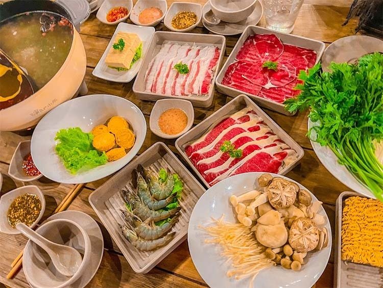 B&agrave;n tiệc lẩu với nhiều loại thực phẩm gồm thịt, t&ocirc;m, nấm v&agrave; rau xanh, k&egrave;m theo gia vị v&agrave; nước chấm.